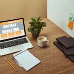 laptop with"content marketing" lettering on screen, notebooks and pencil on wooden tabletop,